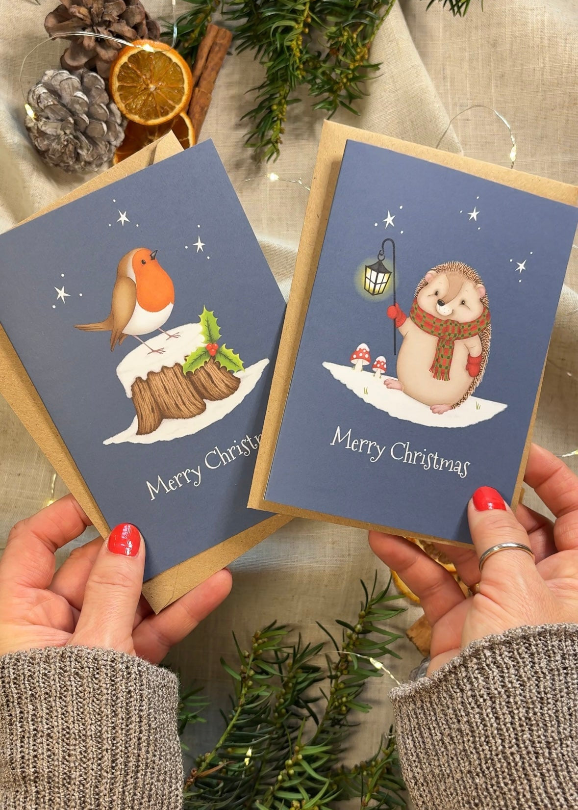 Two Christmas cards held by hands with decorative elements in the background